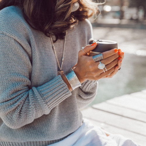 woman holding cup with winter clothing and adorned in embella jewellery